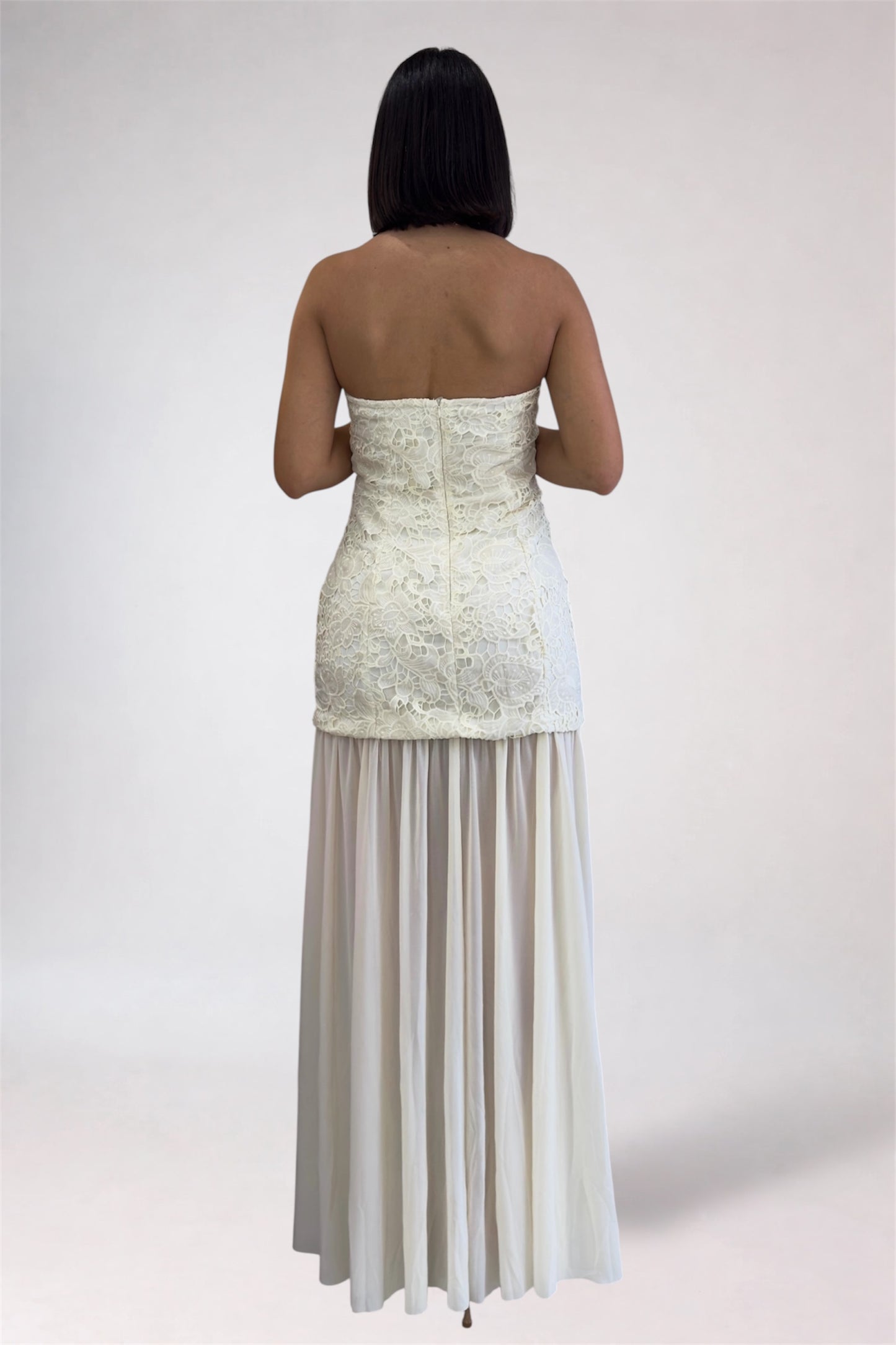 Woman wearing a strapless white lace dress with a plain background