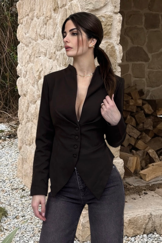 Woman wearing a black blazer over a deep neckline outfit in an outdoor setting.