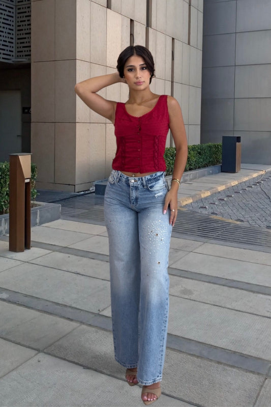 Woman wearing a red top and blue jeans standing on a sidewalk with a building in the background