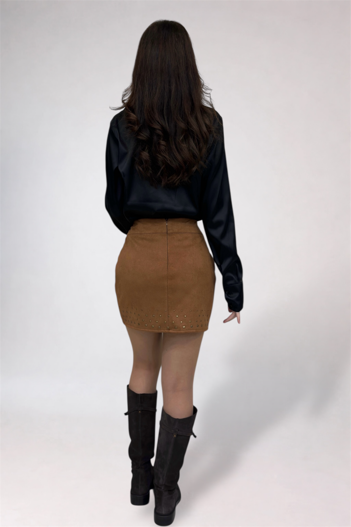 Person wearing a black blouse, brown skirt, and black boots on a white background