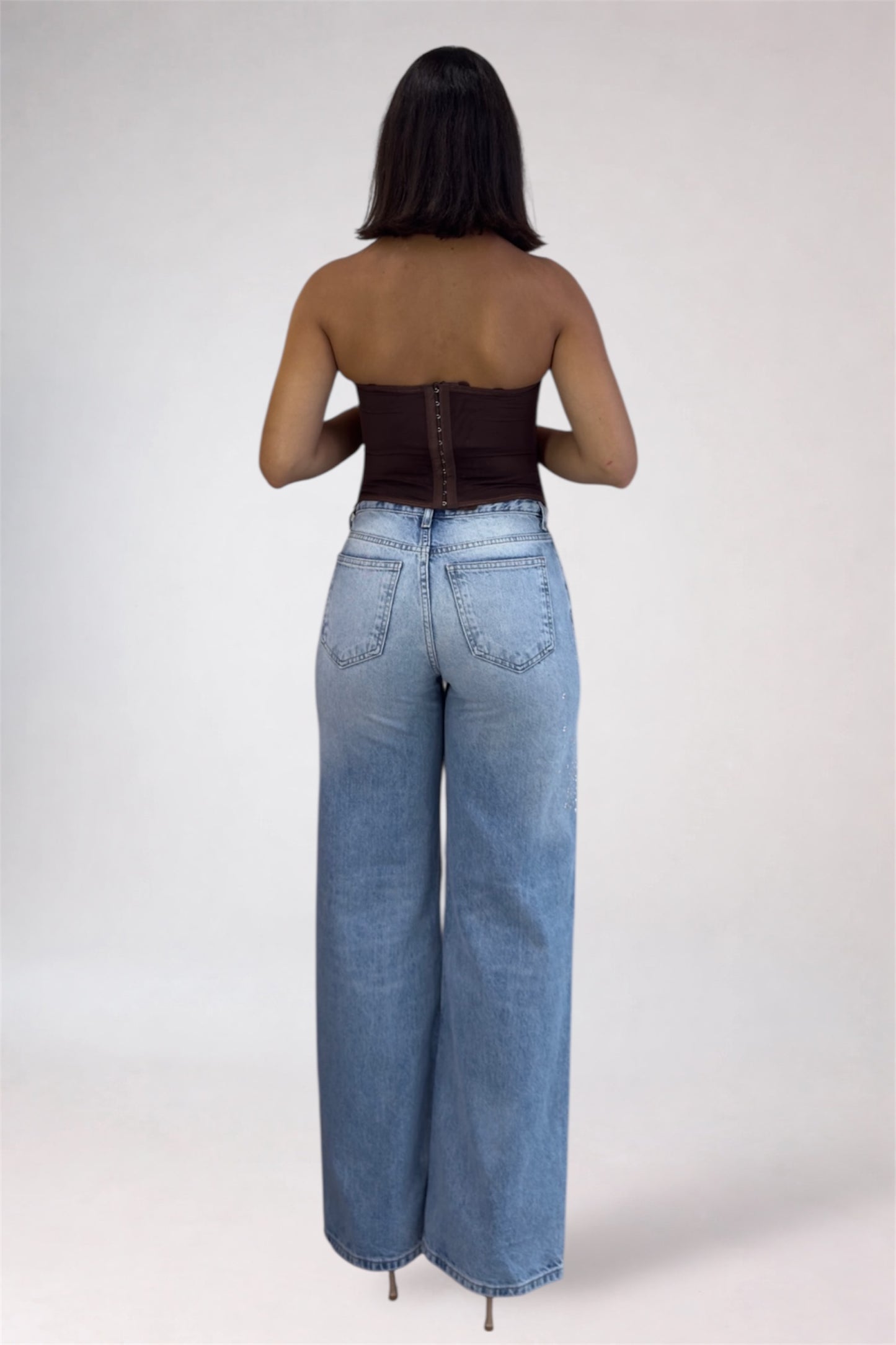 Person wearing high-waisted blue jeans and a strapless top on a white background