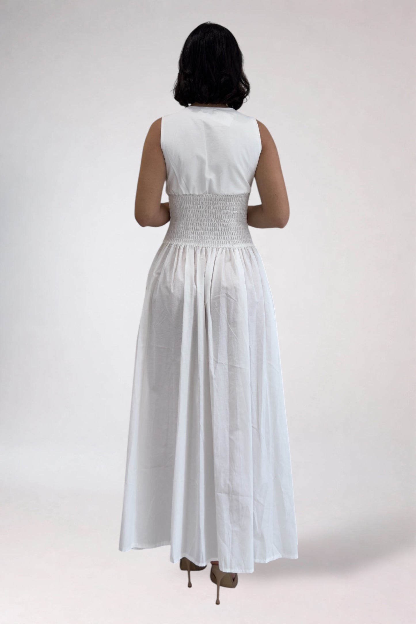 Woman wearing a white sleeveless top and long skirt on a plain background