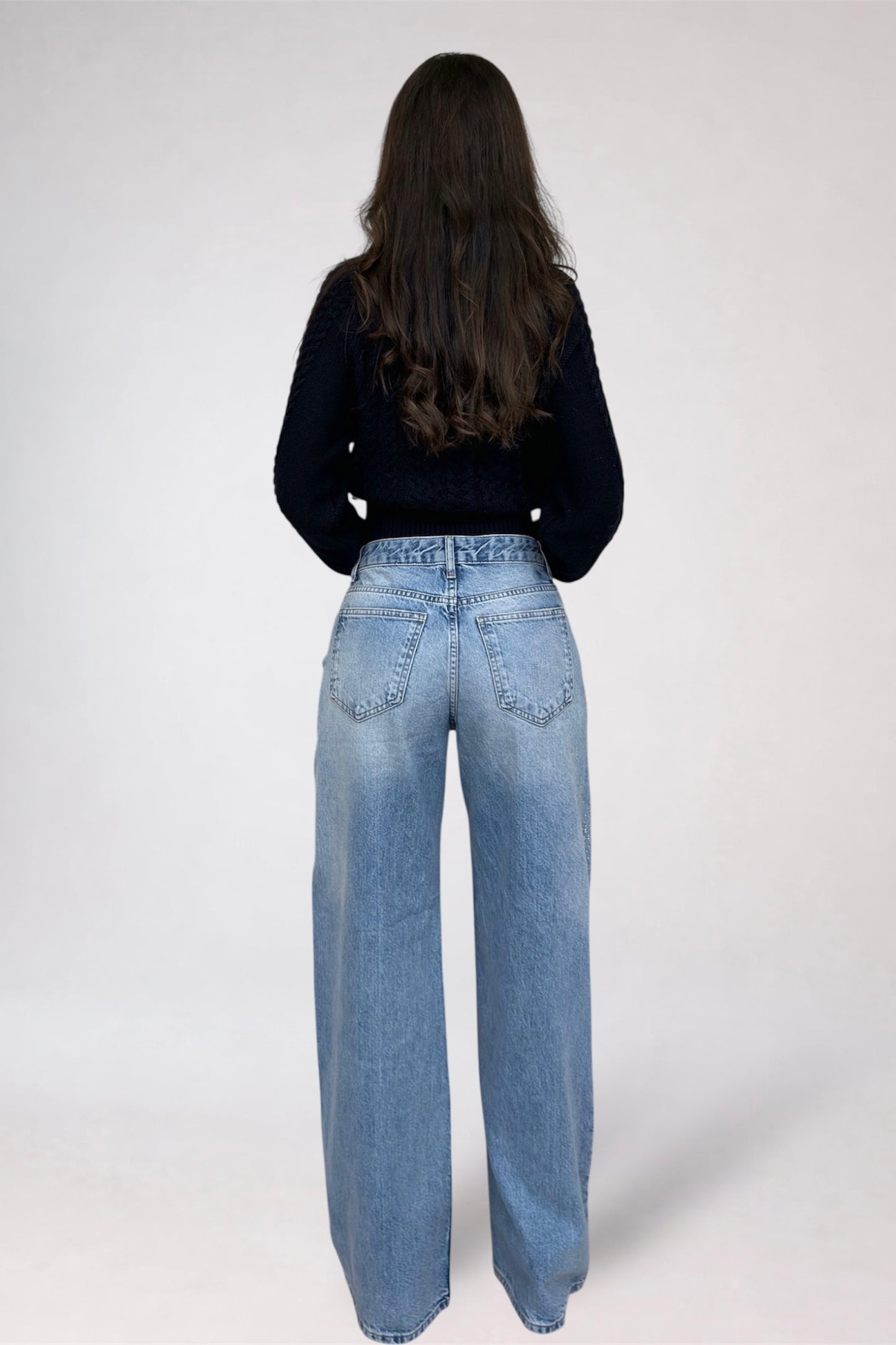 Person wearing blue jeans and a black top on a white background
