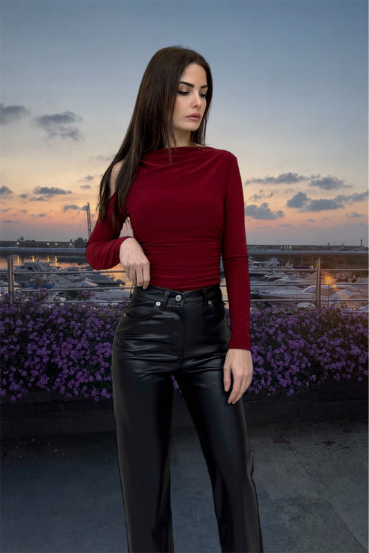 Woman wearing a red top and black pants standing on a rooftop with a cityscape and sunset in the background.