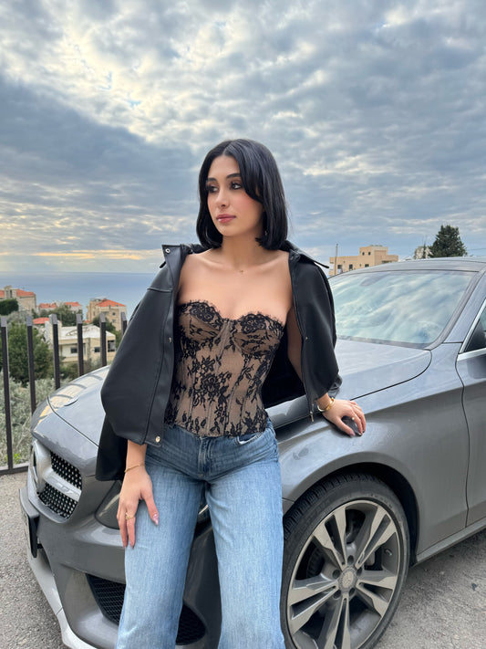 Woman in a lace top and jeans standing next to a car with a scenic background