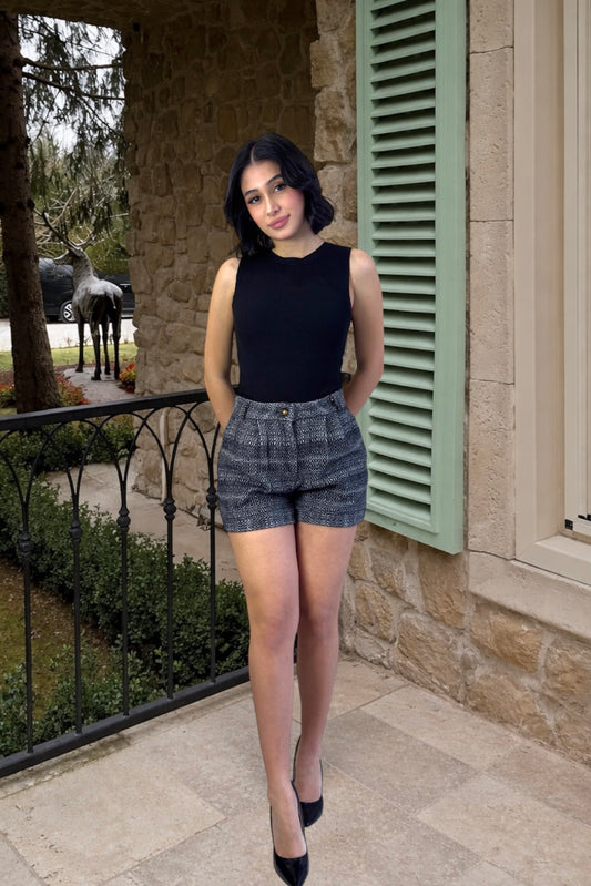 Woman in black sleeveless top and gray shorts standing on a stone porch.