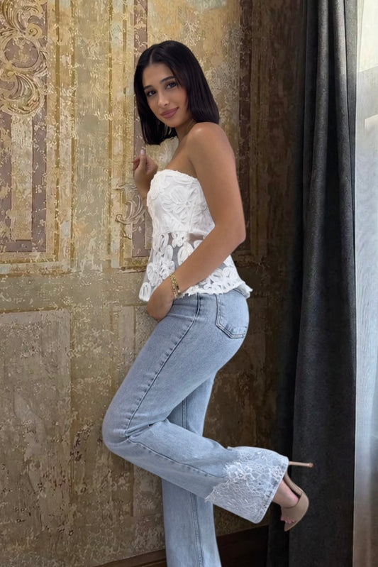 Woman wearing a white lace top and light blue jeans against a textured wall.