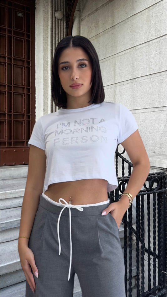 Woman wearing a white t-shirt with text and gray pants standing outdoors.