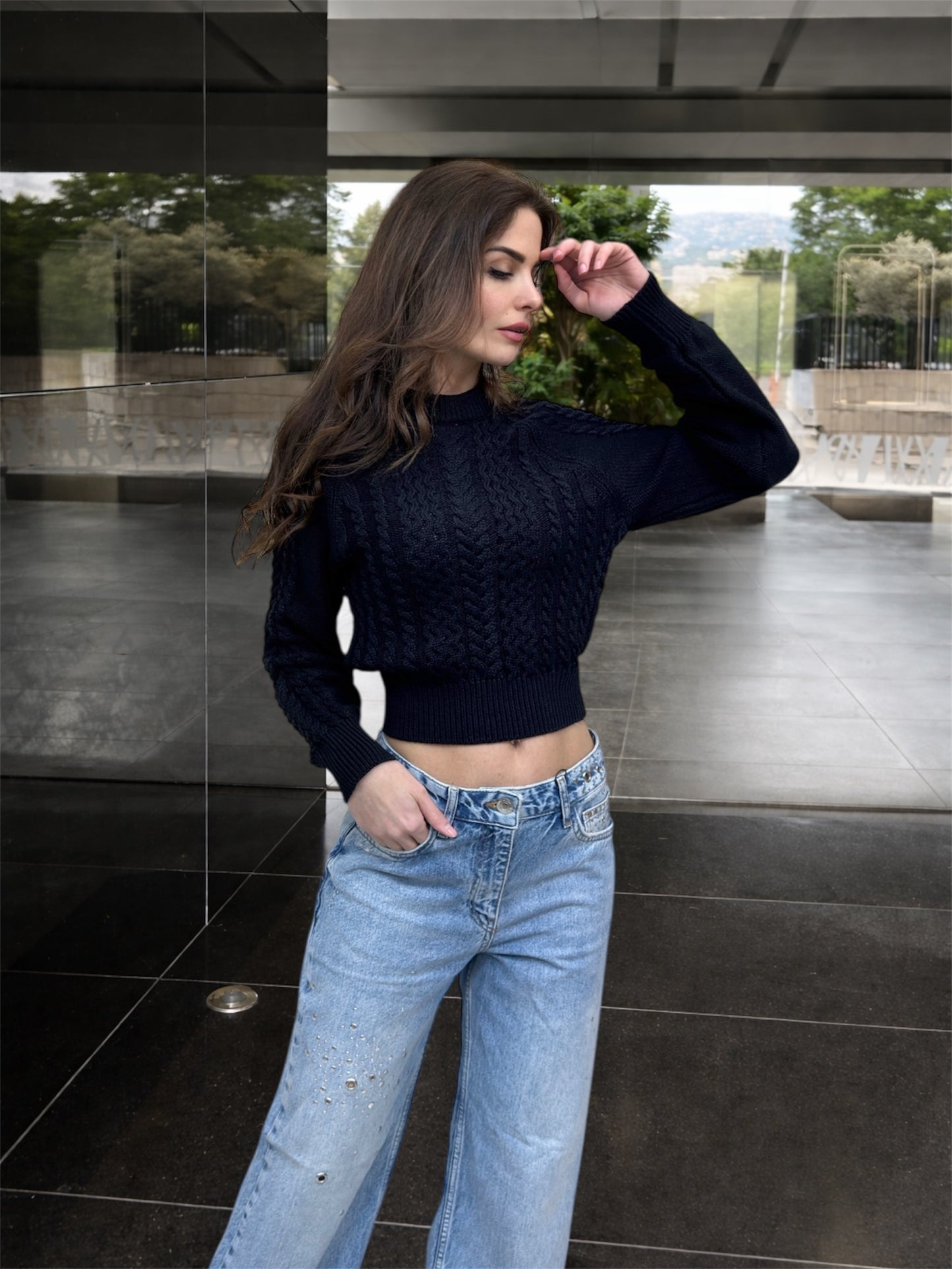 Woman wearing a black sweater and blue jeans standing in an outdoor setting.