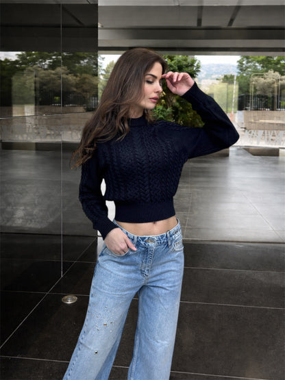 Woman wearing a black sweater and blue jeans standing in an outdoor setting.