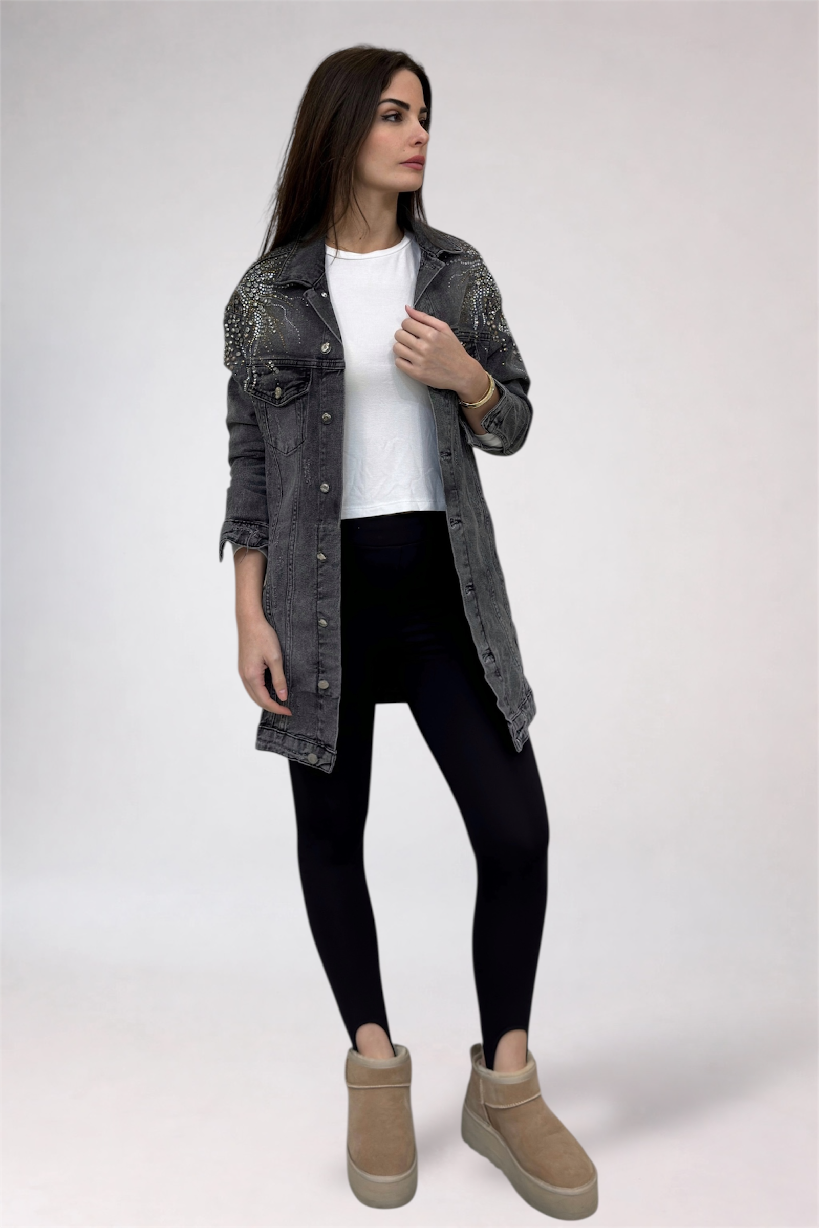 Woman wearing a denim jacket, white shirt, black leggings, and beige boots on a white background