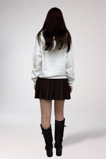 Person wearing a white sweatshirt, pleated skirt, and black boots on a plain background