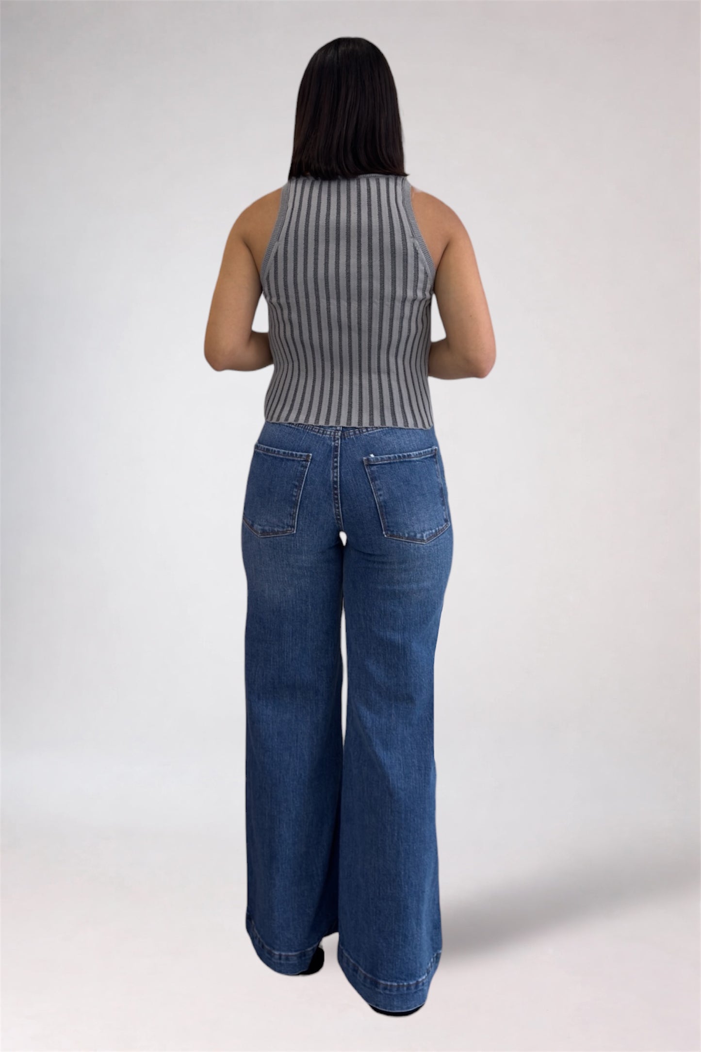 Person wearing a ribbed tank top and blue jeans on a white background