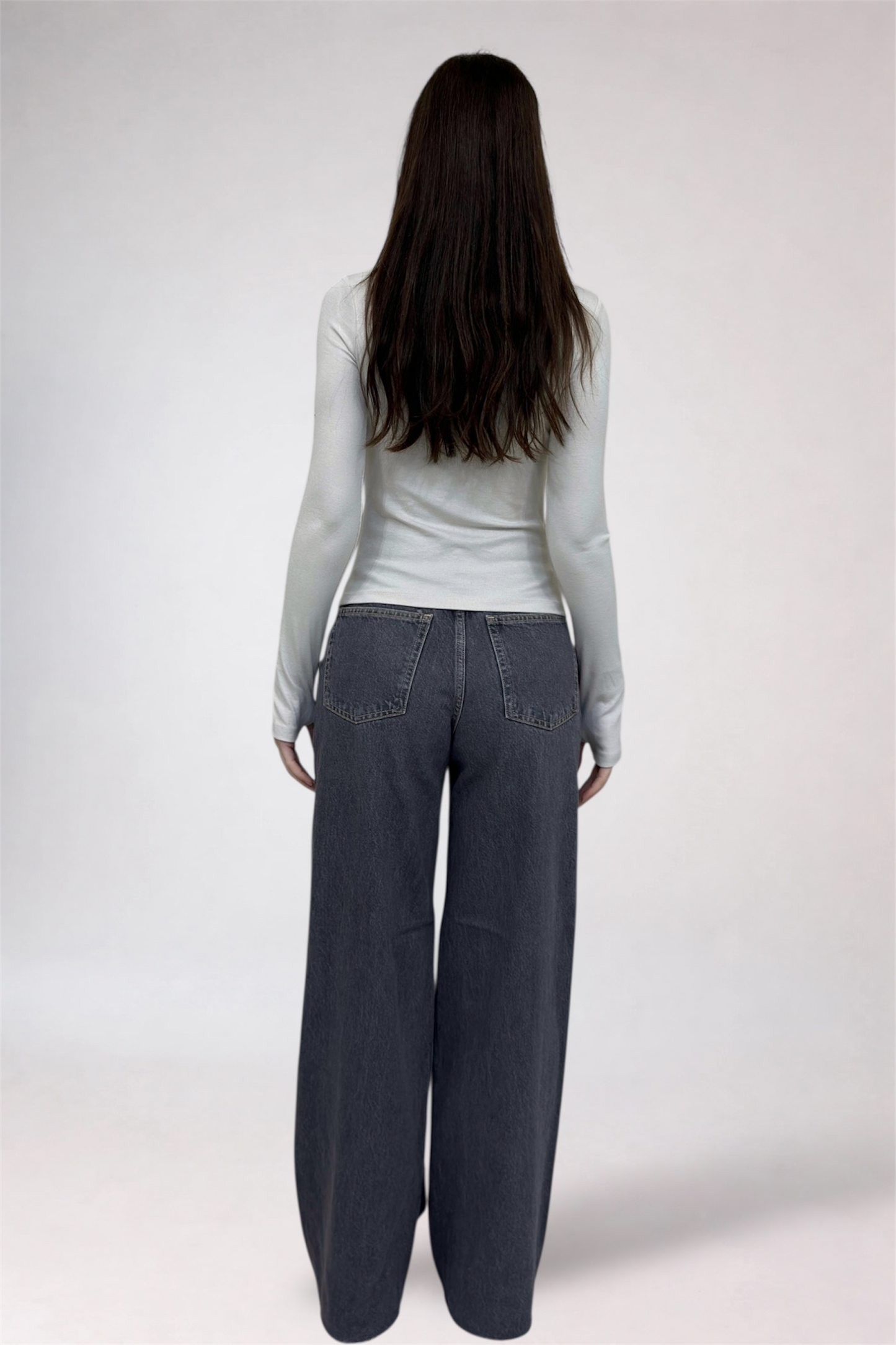 Person wearing a light gray long-sleeve top and dark gray wide-leg pants on a white background