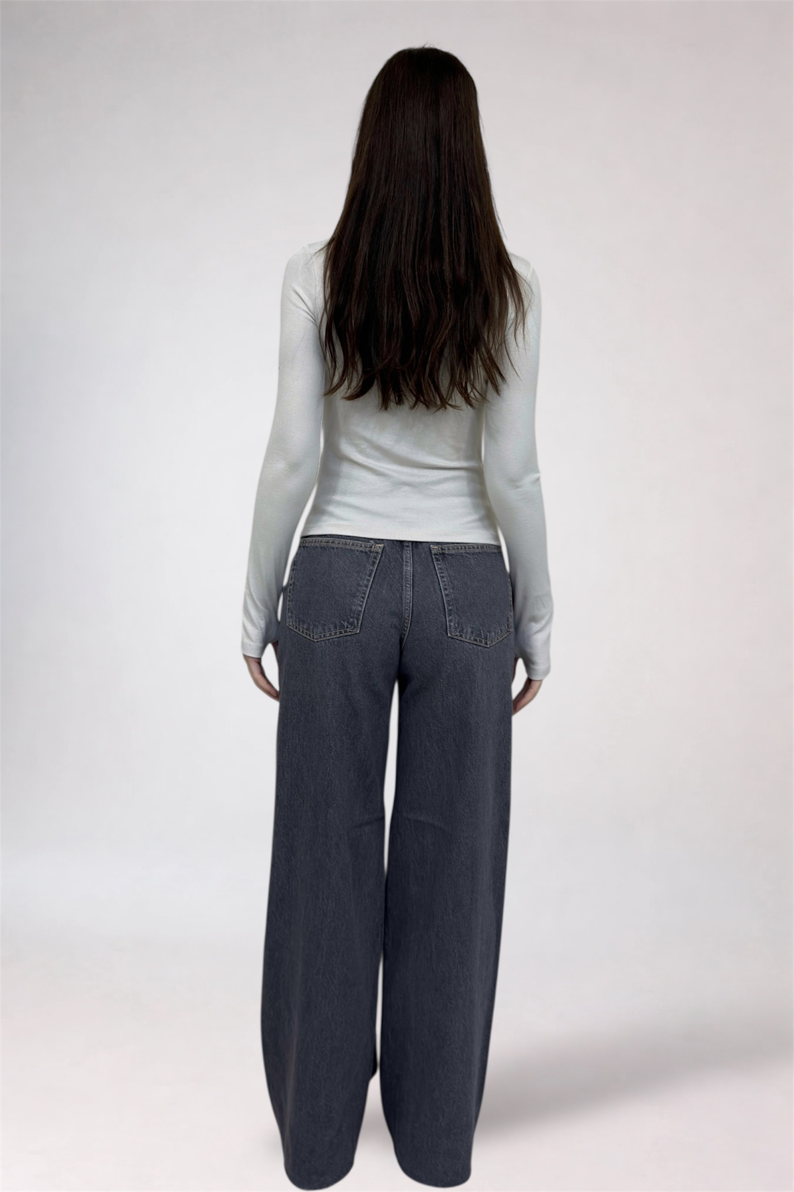 Person wearing a light gray long-sleeve top and dark gray wide-leg pants on a white background
