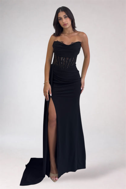 Woman wearing a black strapless gown with a high slit on a white background