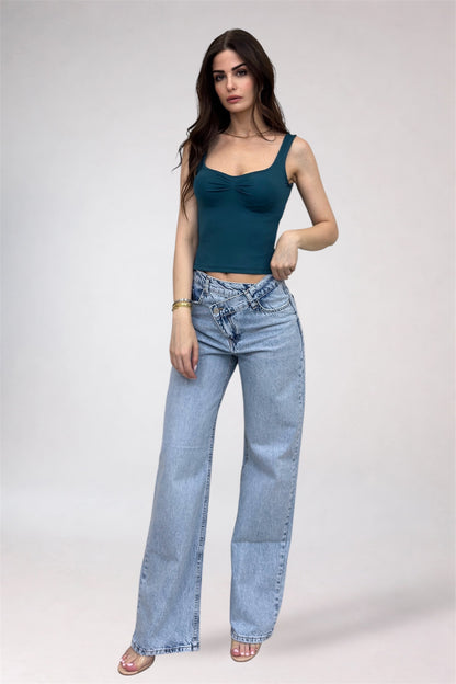 Woman wearing a teal top and light blue jeans on a white background