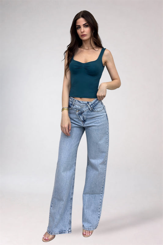 Woman wearing a teal top and light blue jeans on a white background
