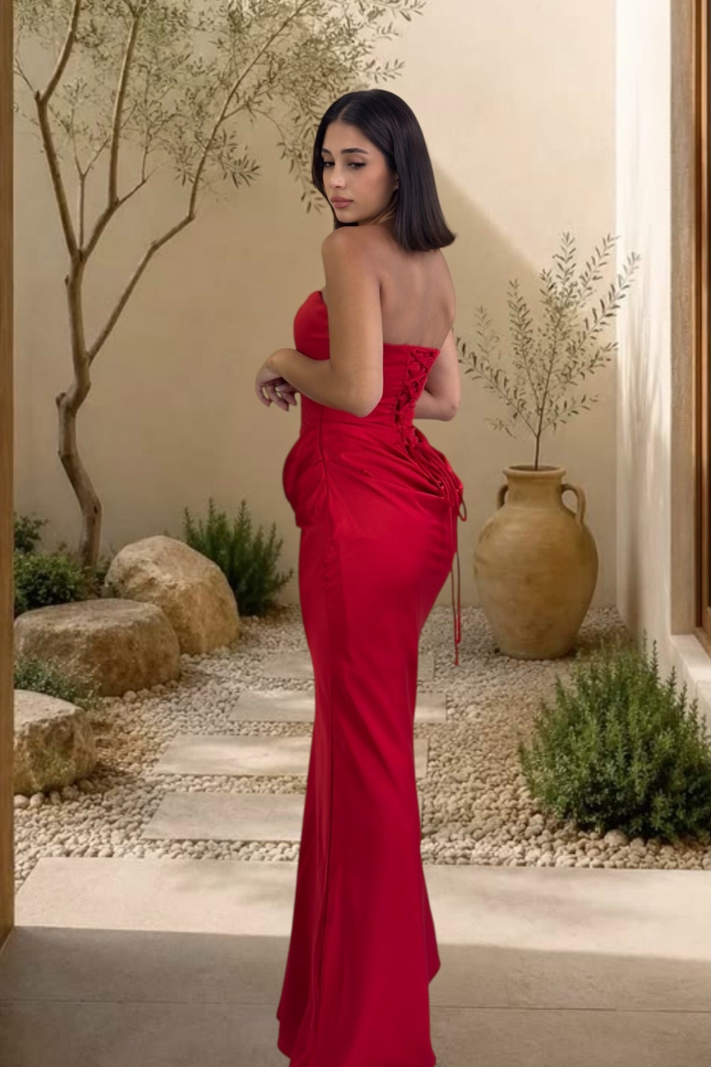 Woman in a red strapless gown standing in an outdoor setting with plants and rocks.