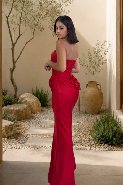 Woman in a red strapless gown standing in an outdoor setting with plants and rocks.
