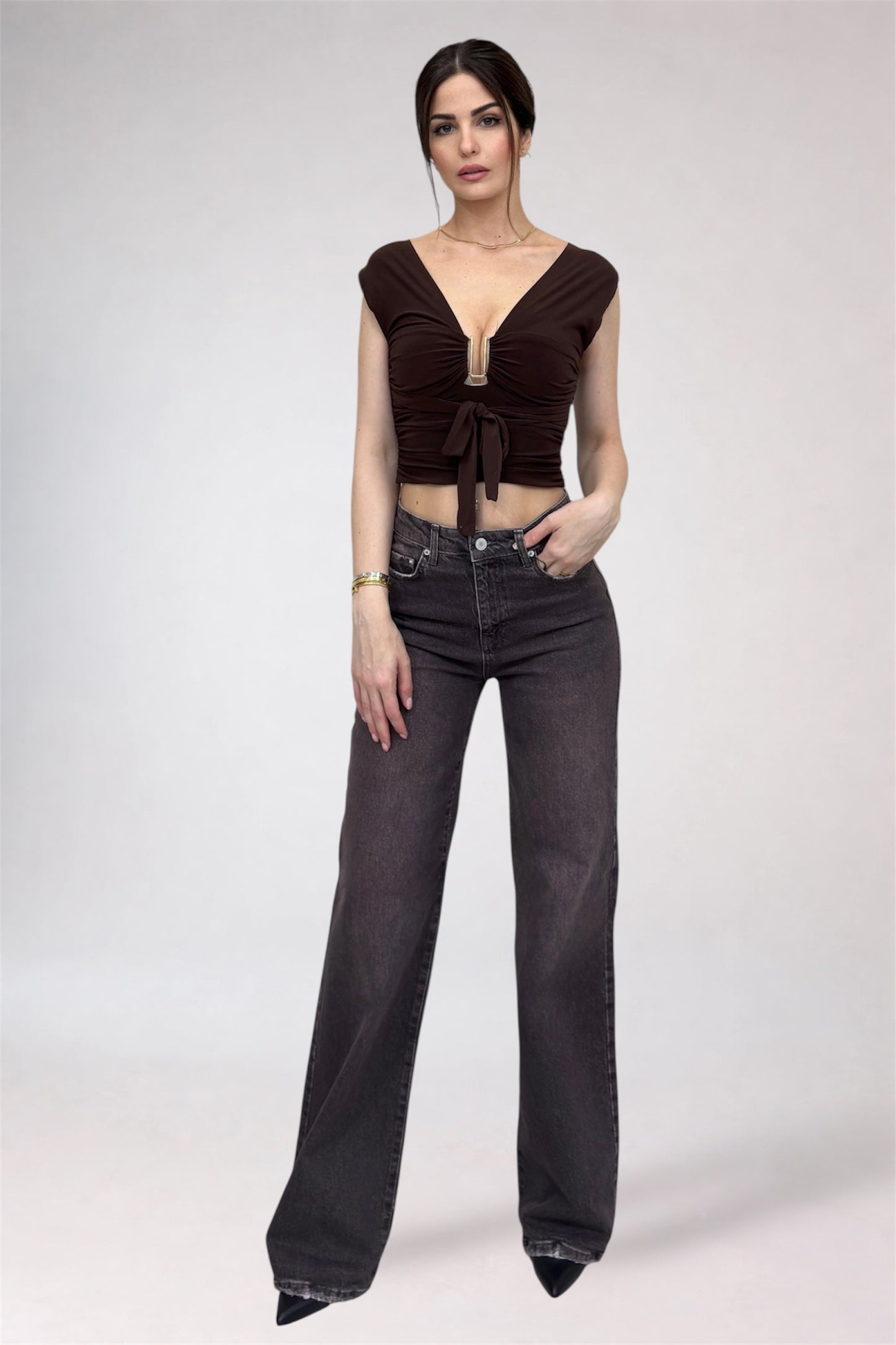 Woman wearing a brown cropped top and black high-waisted jeans on a white background