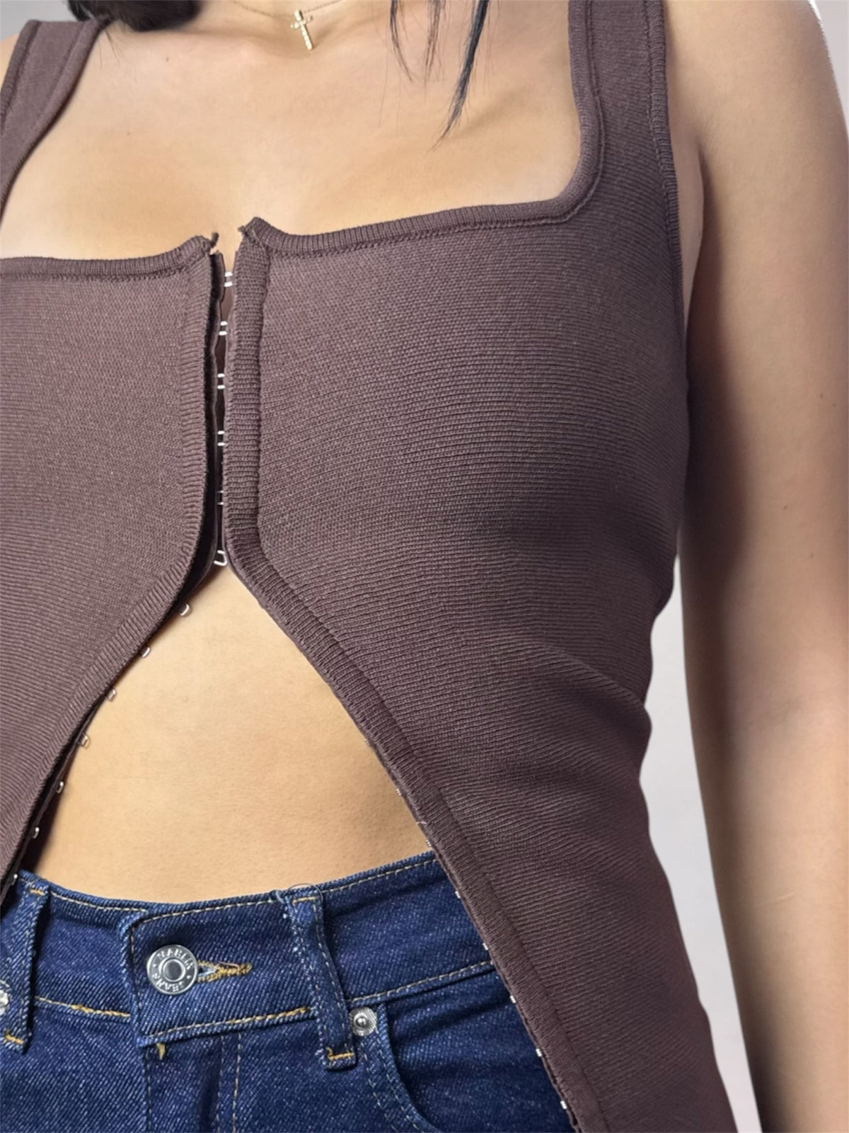 A close-up of a model wearing a ribbed brown sleeveless top with a square neckline and asymmetrical front cutout, paired with blue jeans.