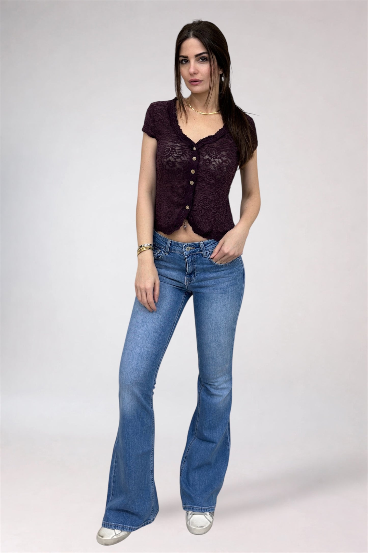 Woman wearing a dark purple lace top and blue jeans on a white background
