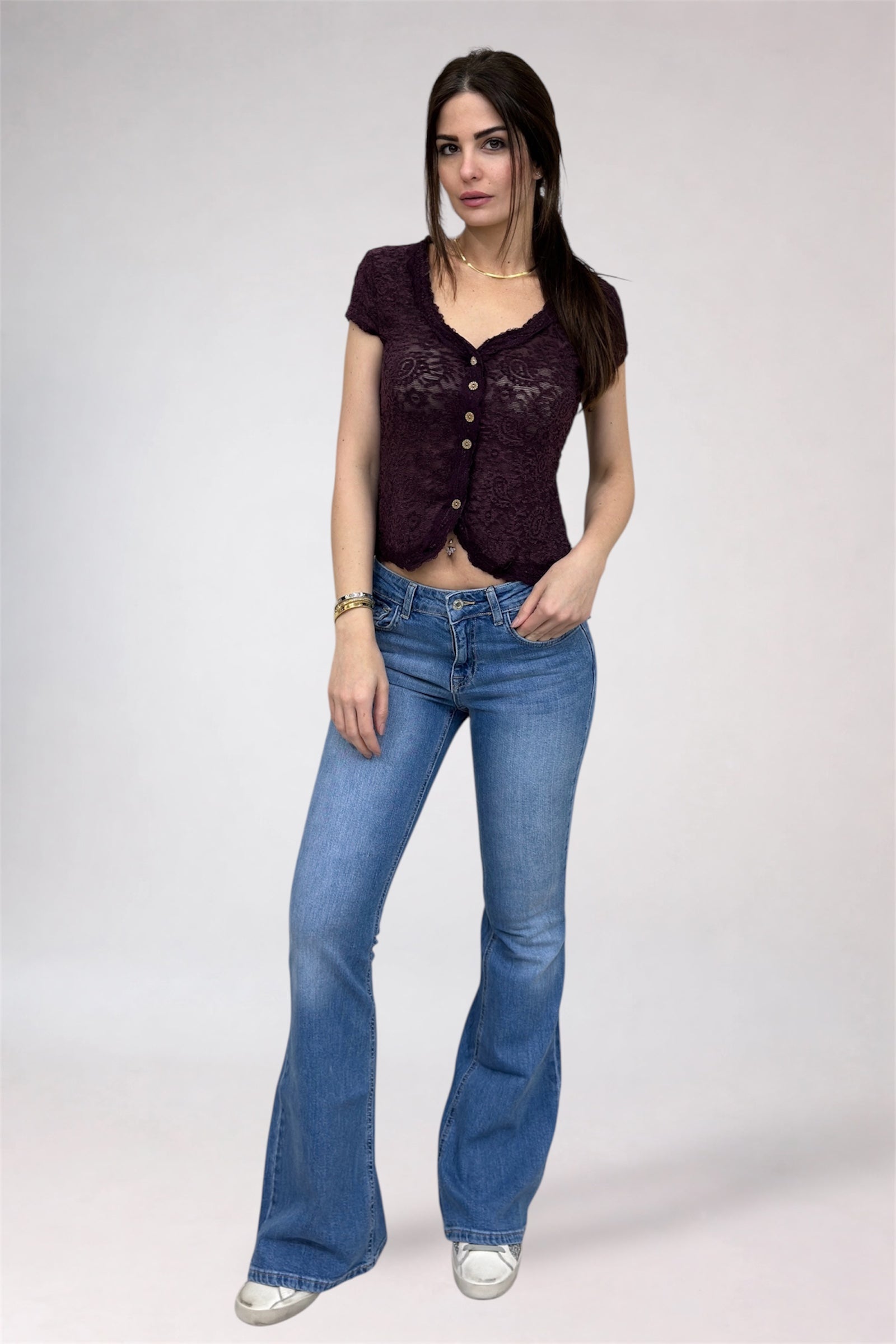 Woman wearing a dark purple lace top and blue jeans on a white background