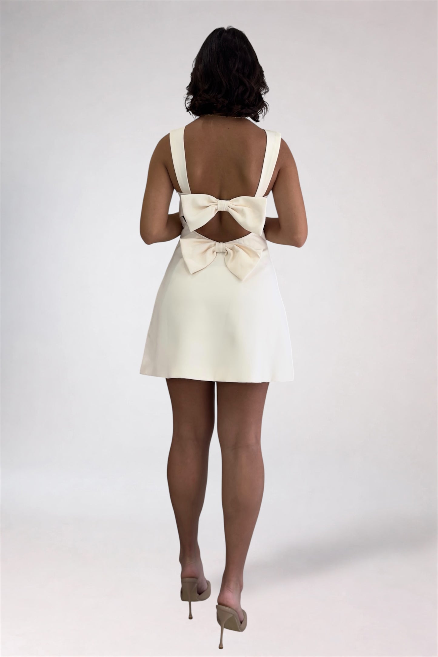 Woman wearing a white dress with a large bow at the back on a plain background