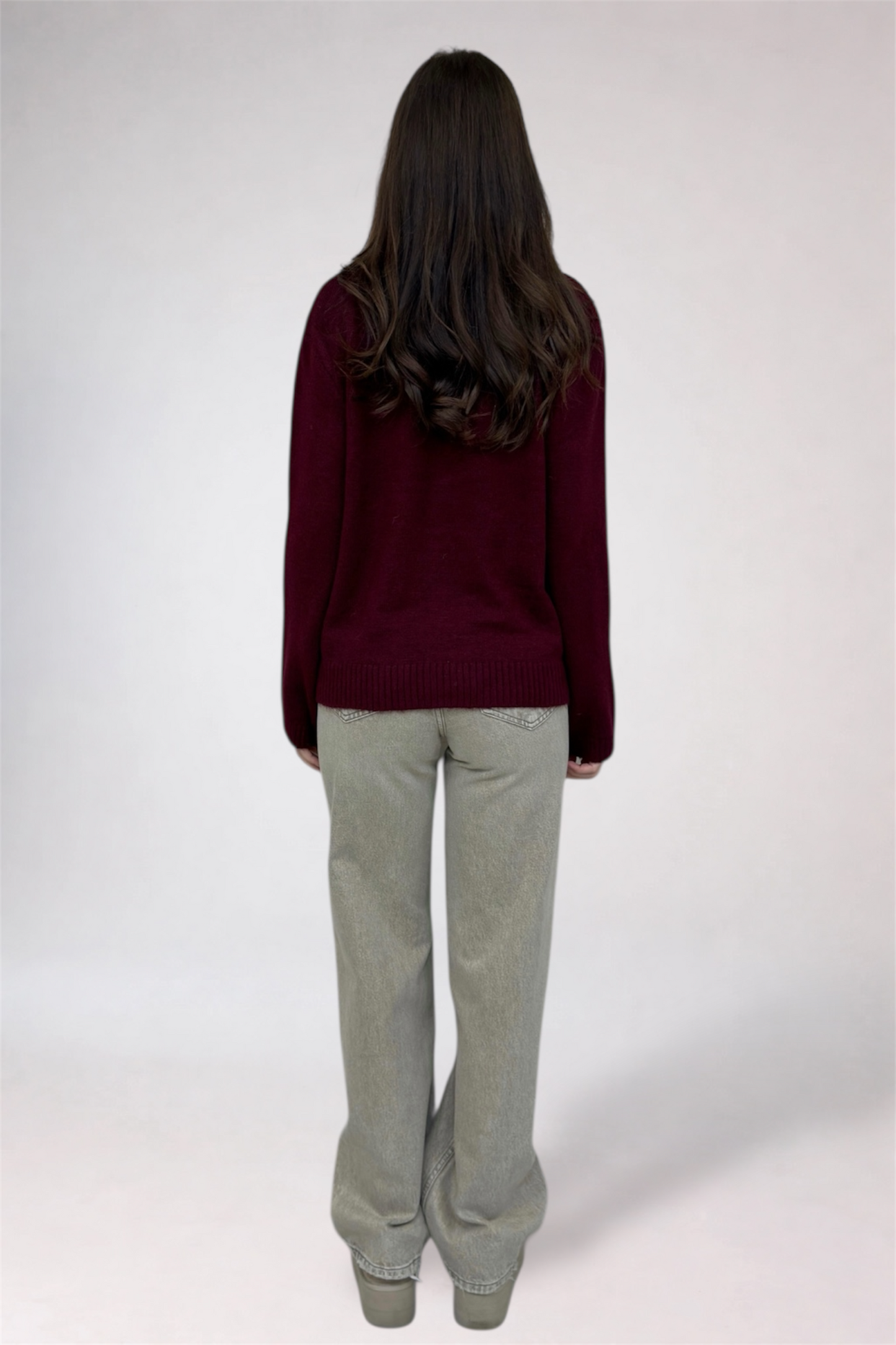 Person wearing a burgundy sweater and light gray pants on a white background