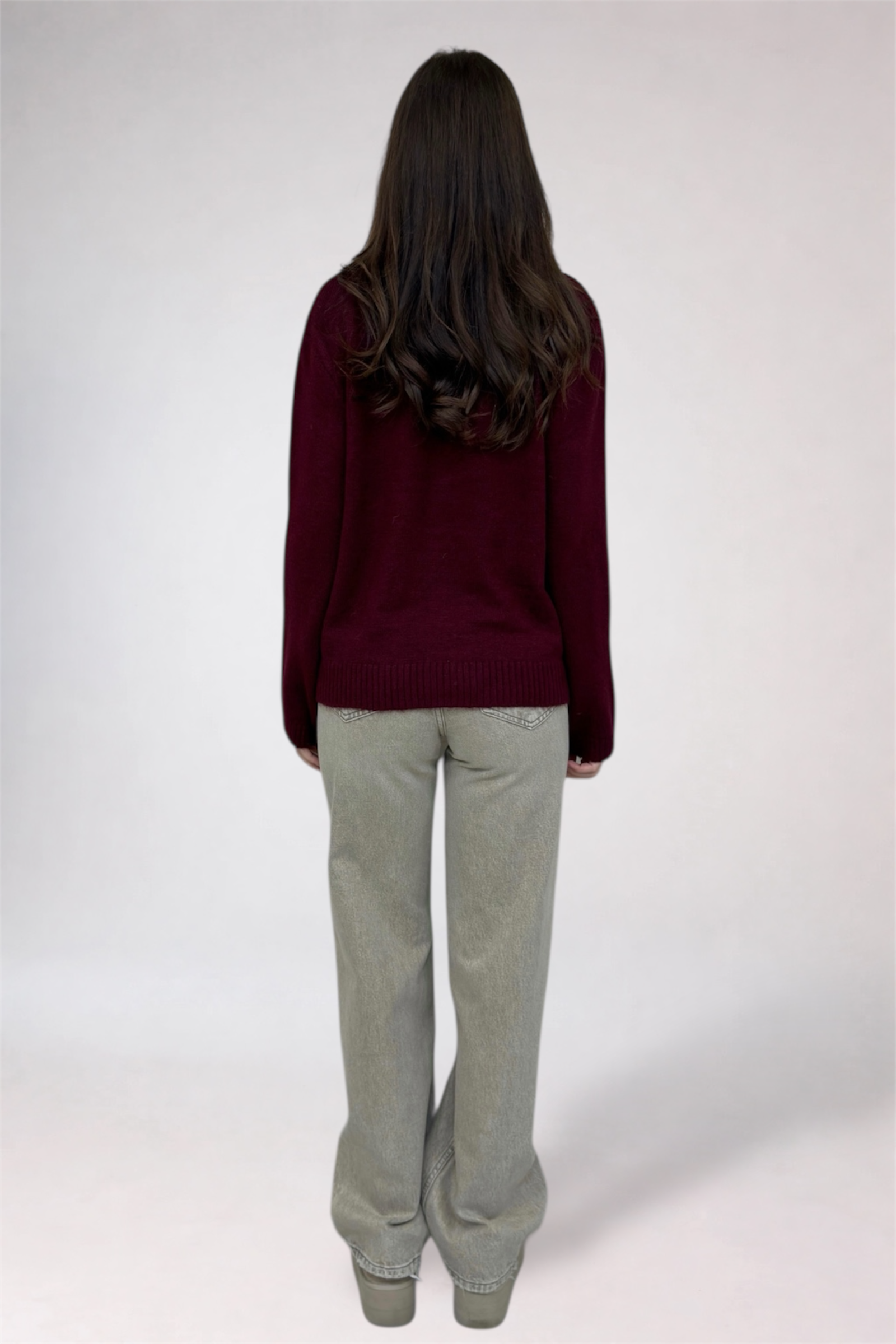 Person wearing a burgundy sweater and light gray pants on a white background