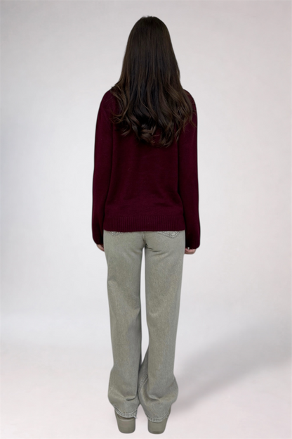 Person wearing a burgundy sweater and light gray pants on a white background