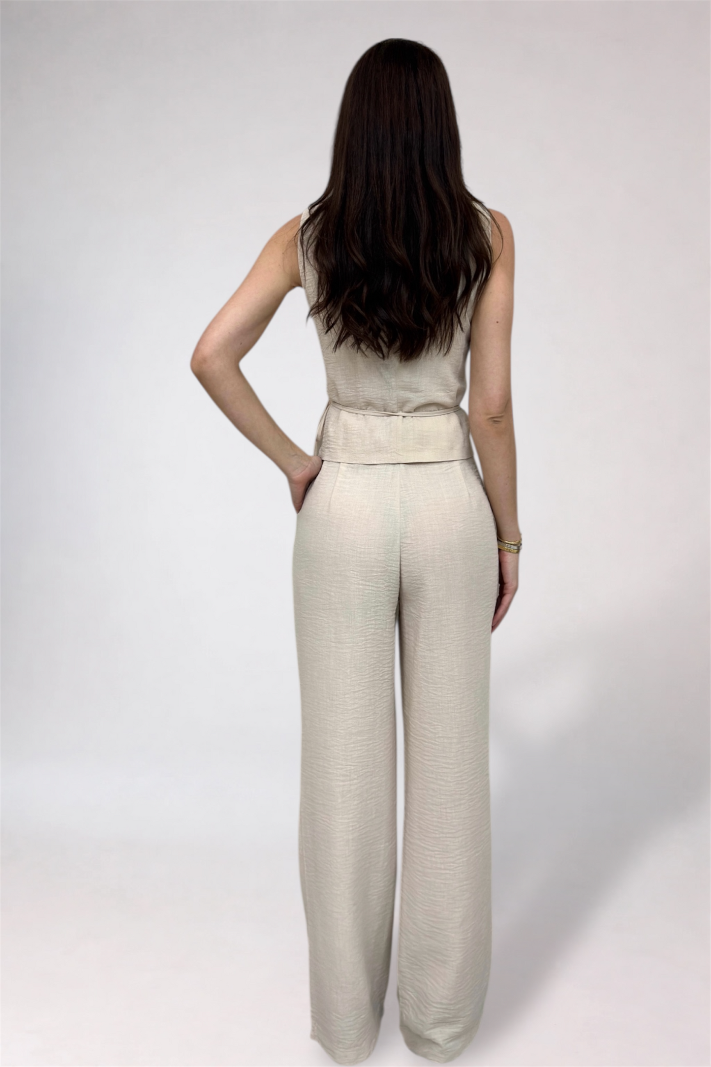 Woman wearing a beige sleeveless top and wide-leg pants on a white background