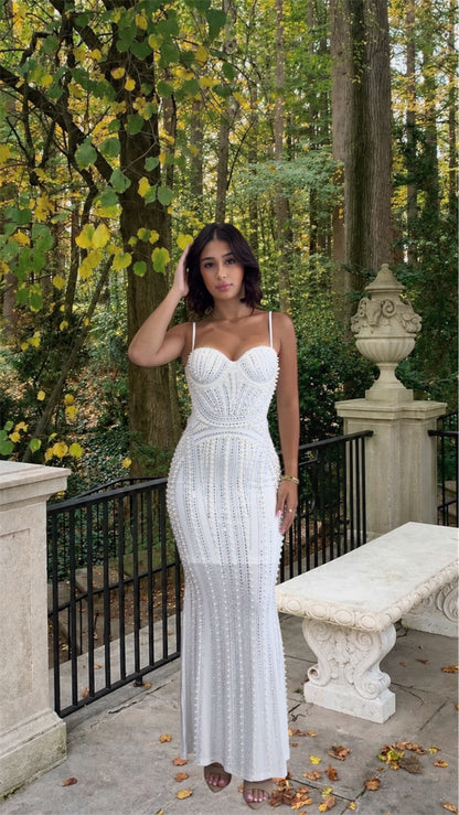 Woman in a white dress standing in a forested area with trees and a bench.