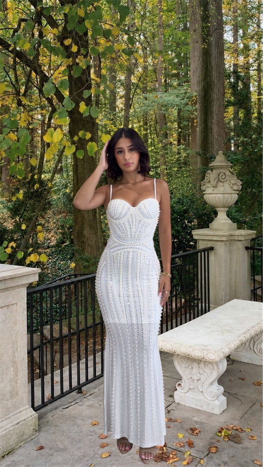 Woman in a white dress standing in a forested area with trees and a bench.
