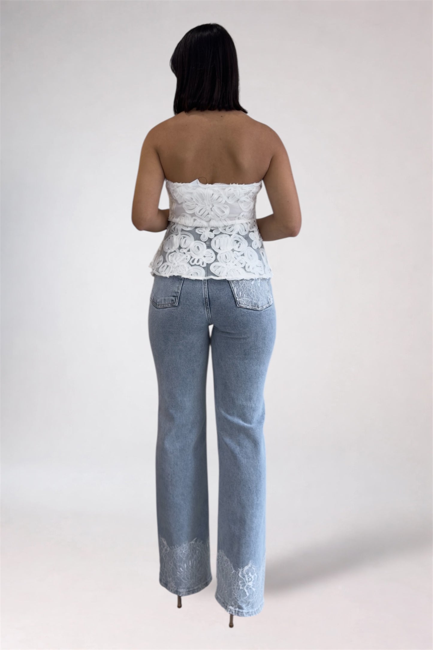Woman wearing a white lace top and light blue jeans on a plain background