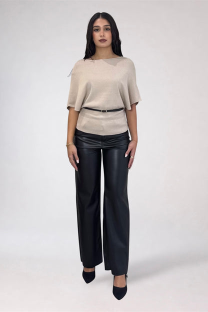 A woman modeling a light beige short-sleeve top with a thin black belt and black wide-leg pants, standing against a plain light gray studio background.