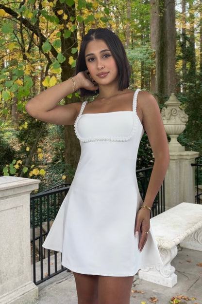 Woman in a white dress standing outdoors with trees and a bench in the background