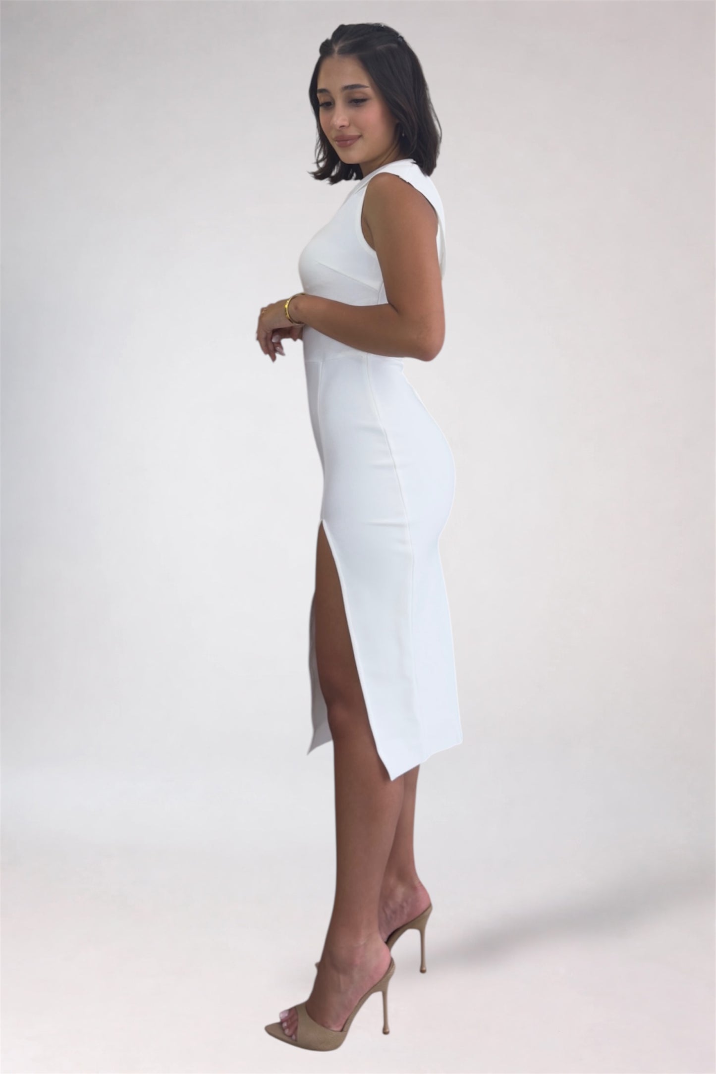 Woman wearing a white sleeveless dress with a slit on a plain background