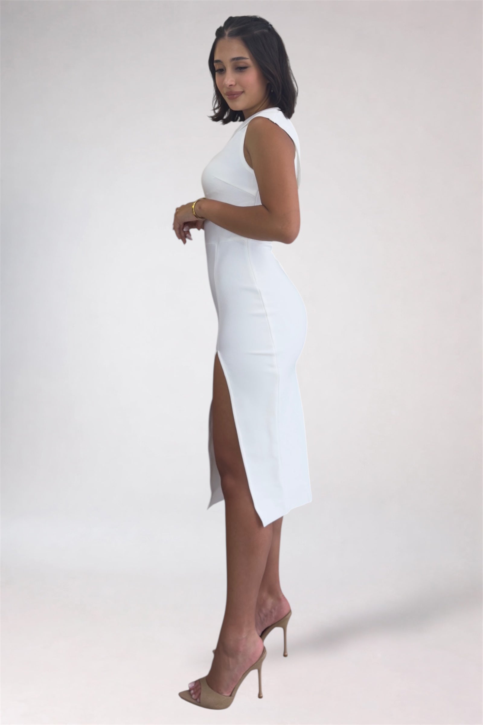 Woman wearing a white sleeveless dress with a slit on a plain background
