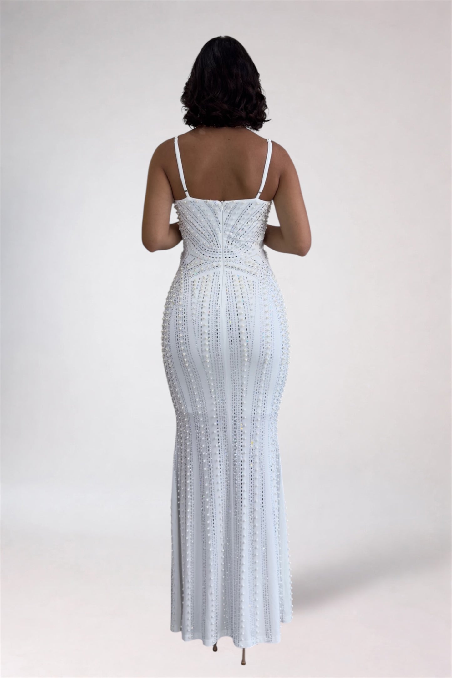Woman wearing a white beaded evening gown against a plain background