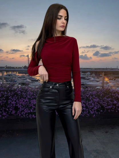 Woman in a red top and black pants standing in front of a scenic background with purple flowers and a sunset.