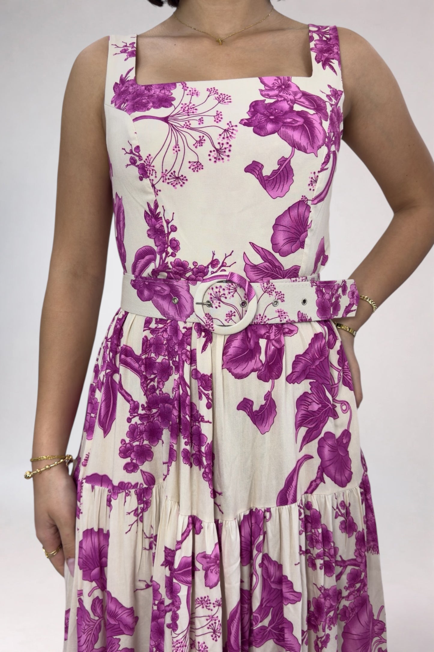 Woman wearing a sleeveless dress with purple floral pattern on a plain background
