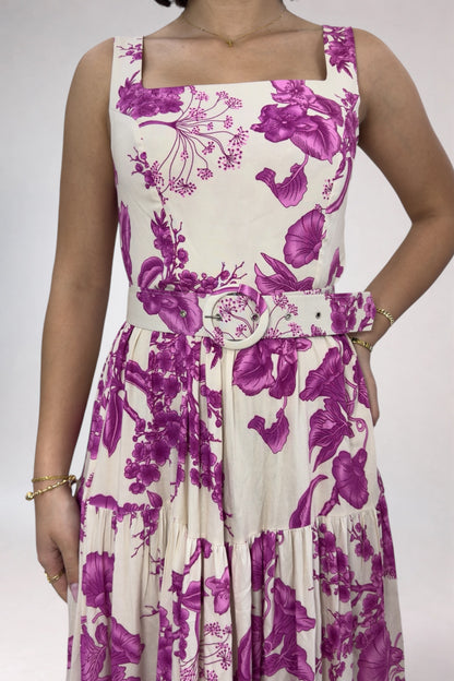 Woman wearing a sleeveless dress with purple floral pattern on a plain background