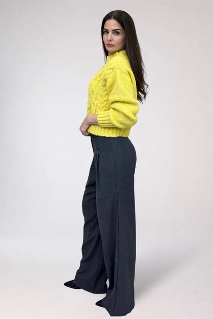 Woman wearing a bright yellow sweater and dark gray pants on a white background