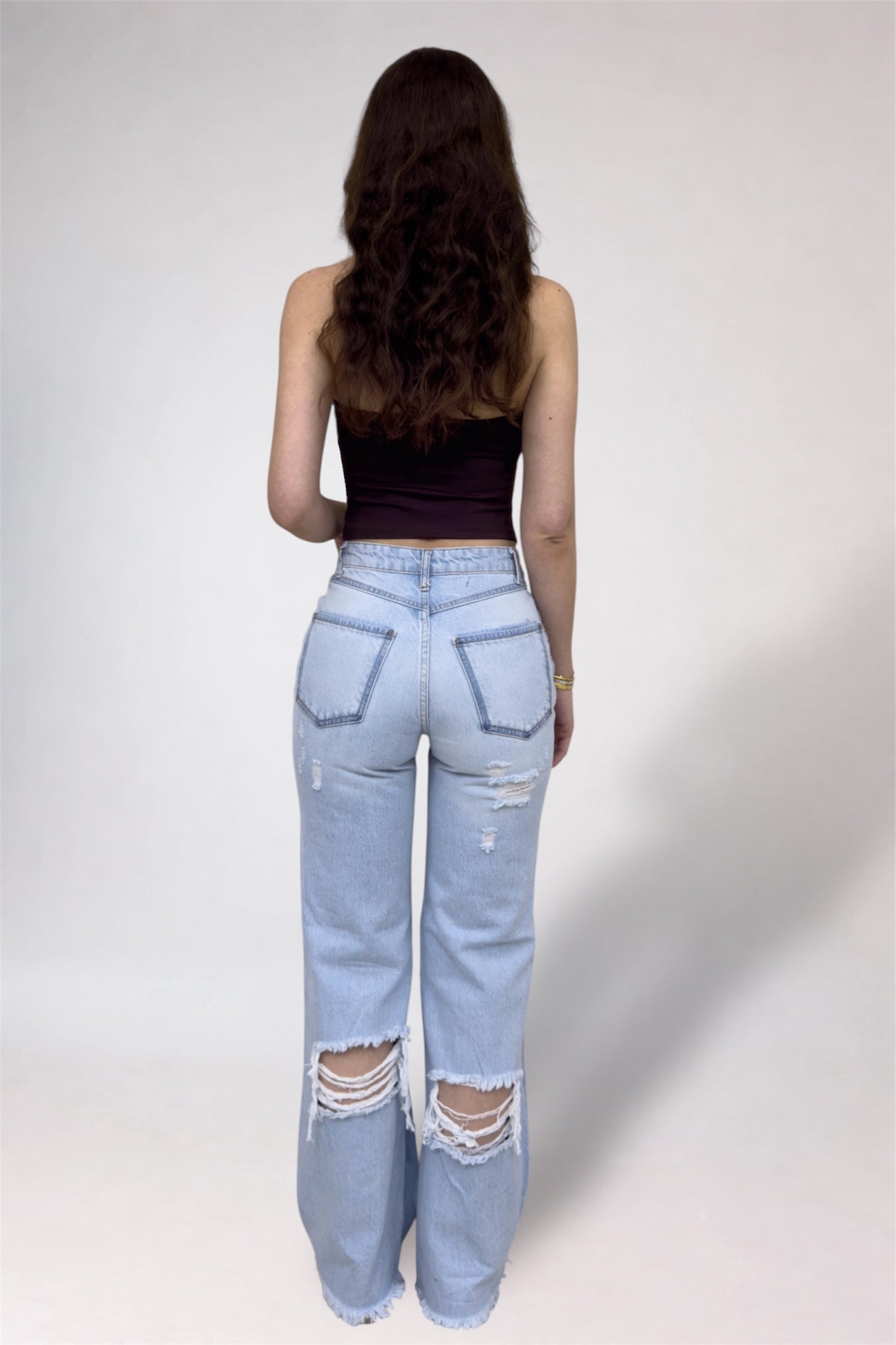Person wearing light blue distressed jeans and a black top on a plain background