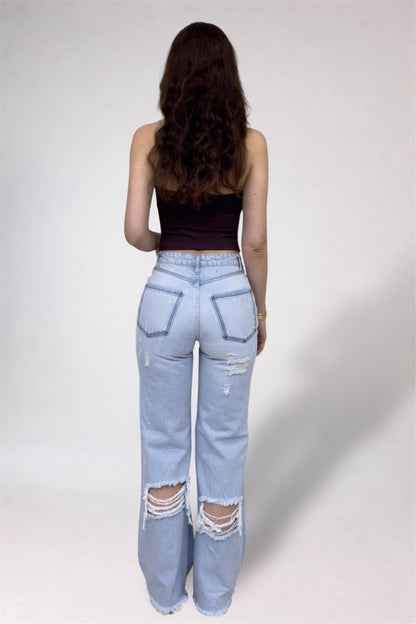Person wearing light blue distressed jeans and a black top on a plain background
