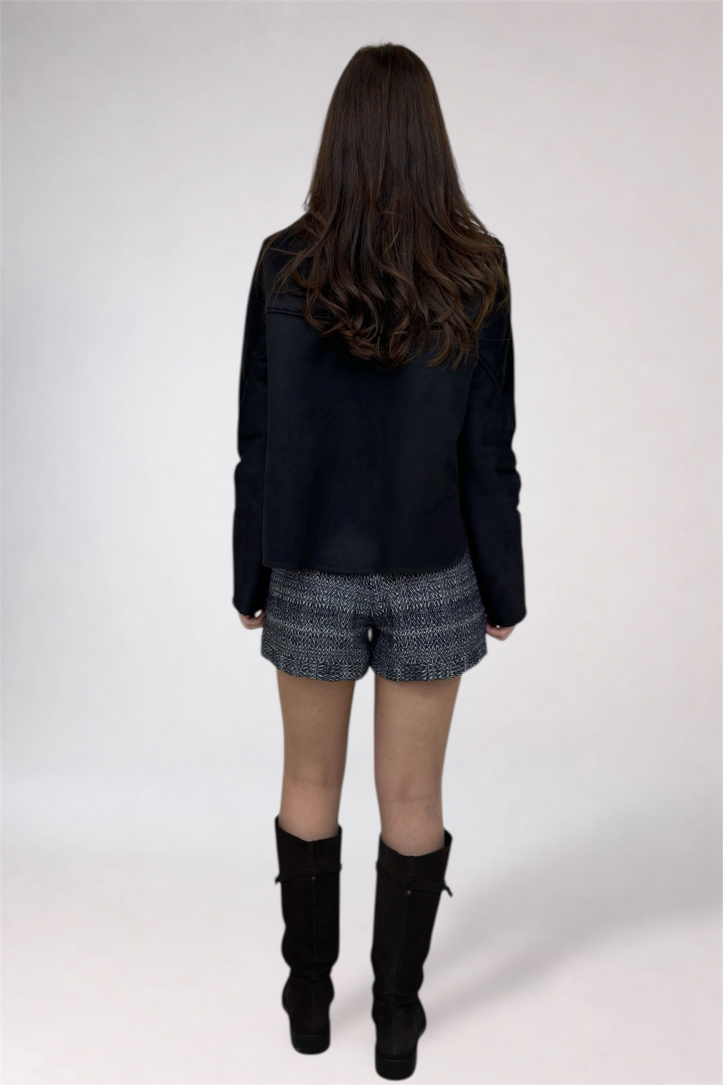Person wearing a black jacket, gray shorts, and black boots on a white background