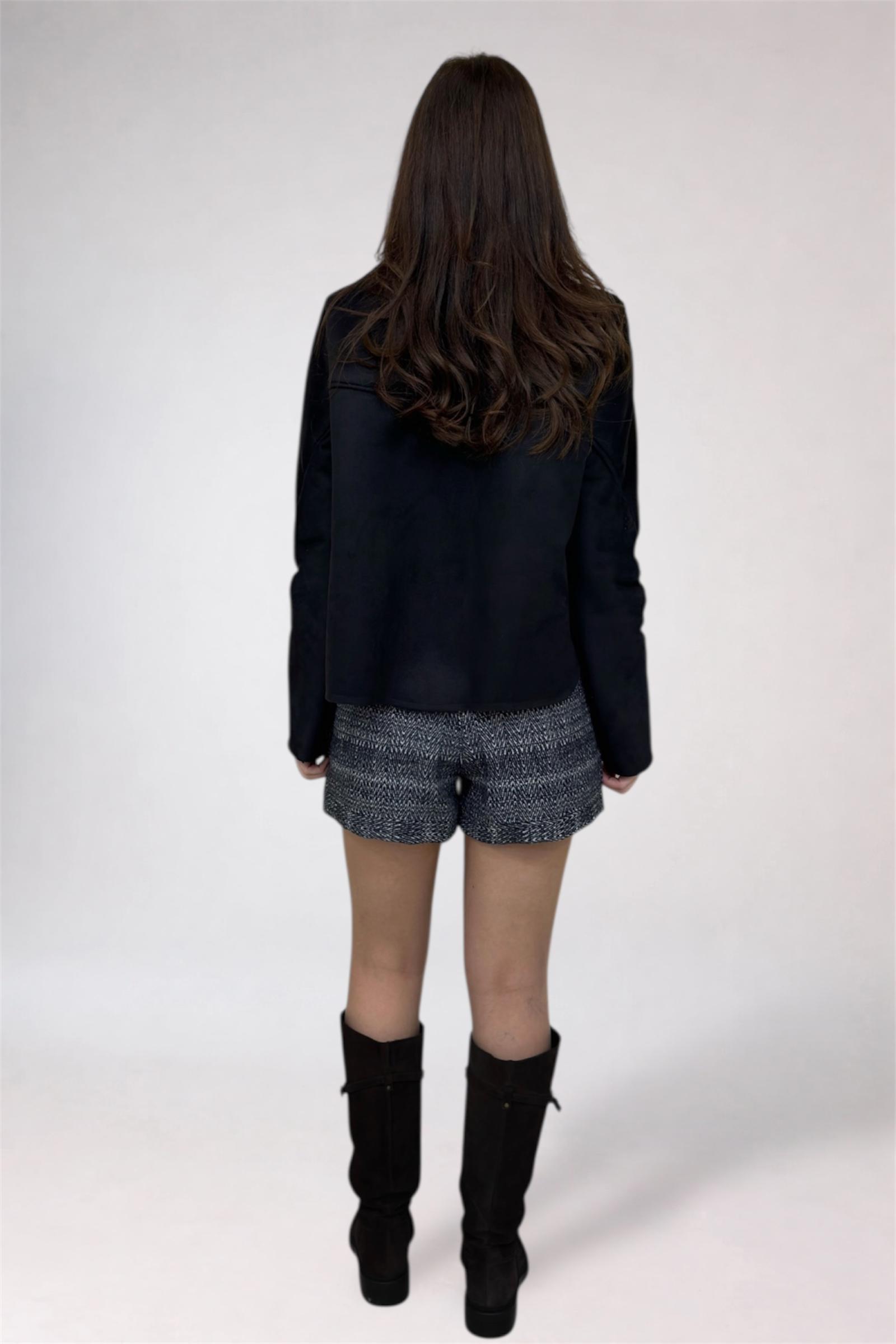 Person wearing a black jacket, gray shorts, and black boots on a white background