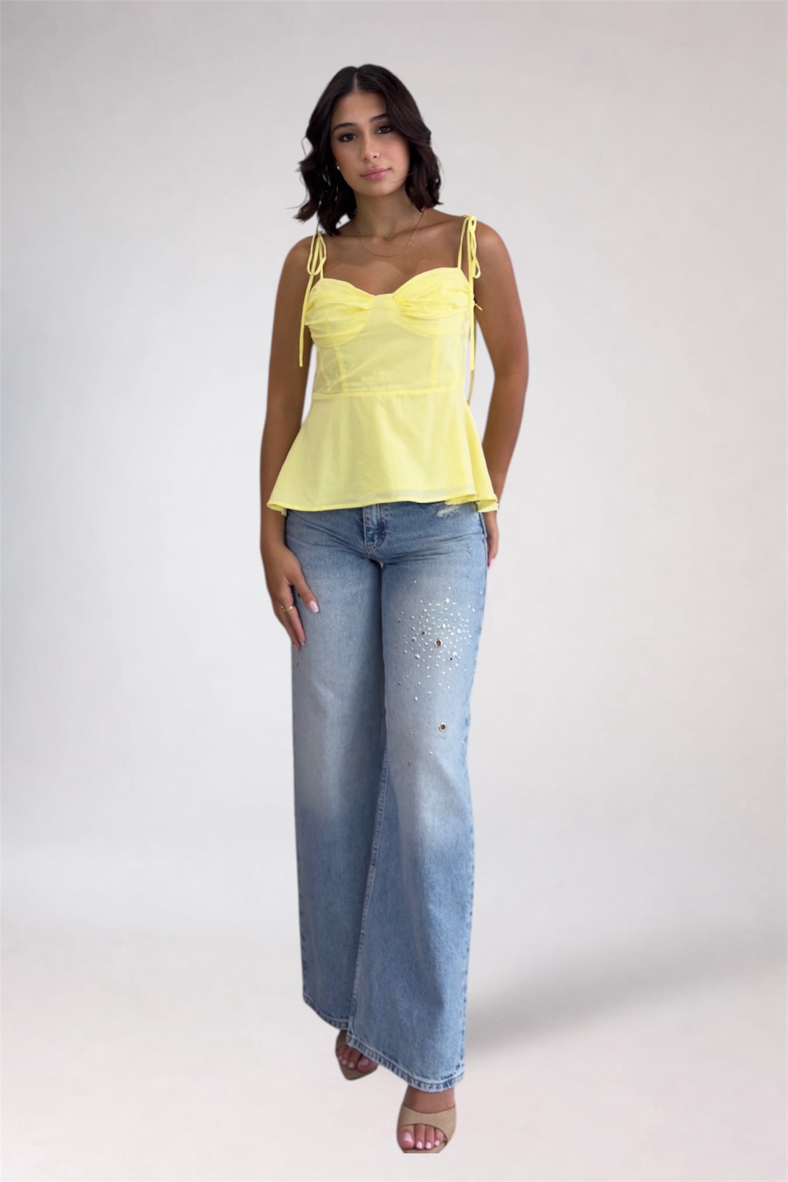 Woman wearing a yellow top and blue jeans on a white background